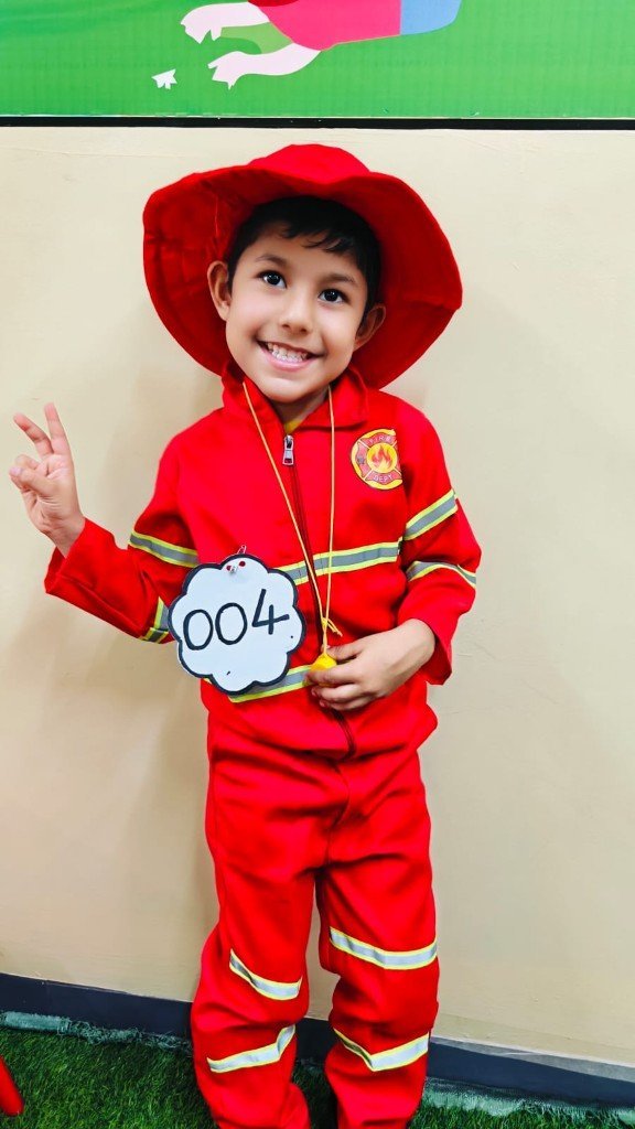 Child in firefighter costume smiling with a peace sign at Galaxy Infant School