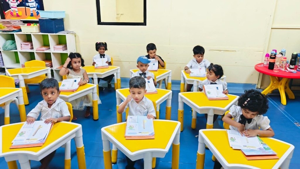 Pre-KG Active Learners in classroom at yellow desks with notebooks